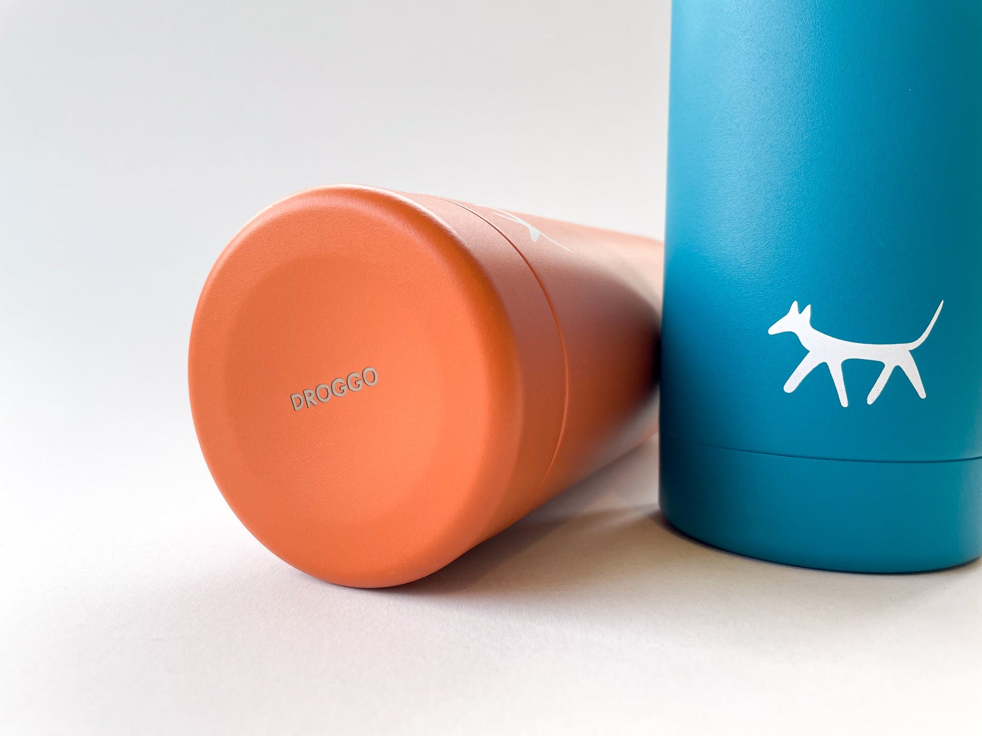 Detail of the Droggo logos at the bottom of the rust water bottle and at the front of the lake water bottle. White background.