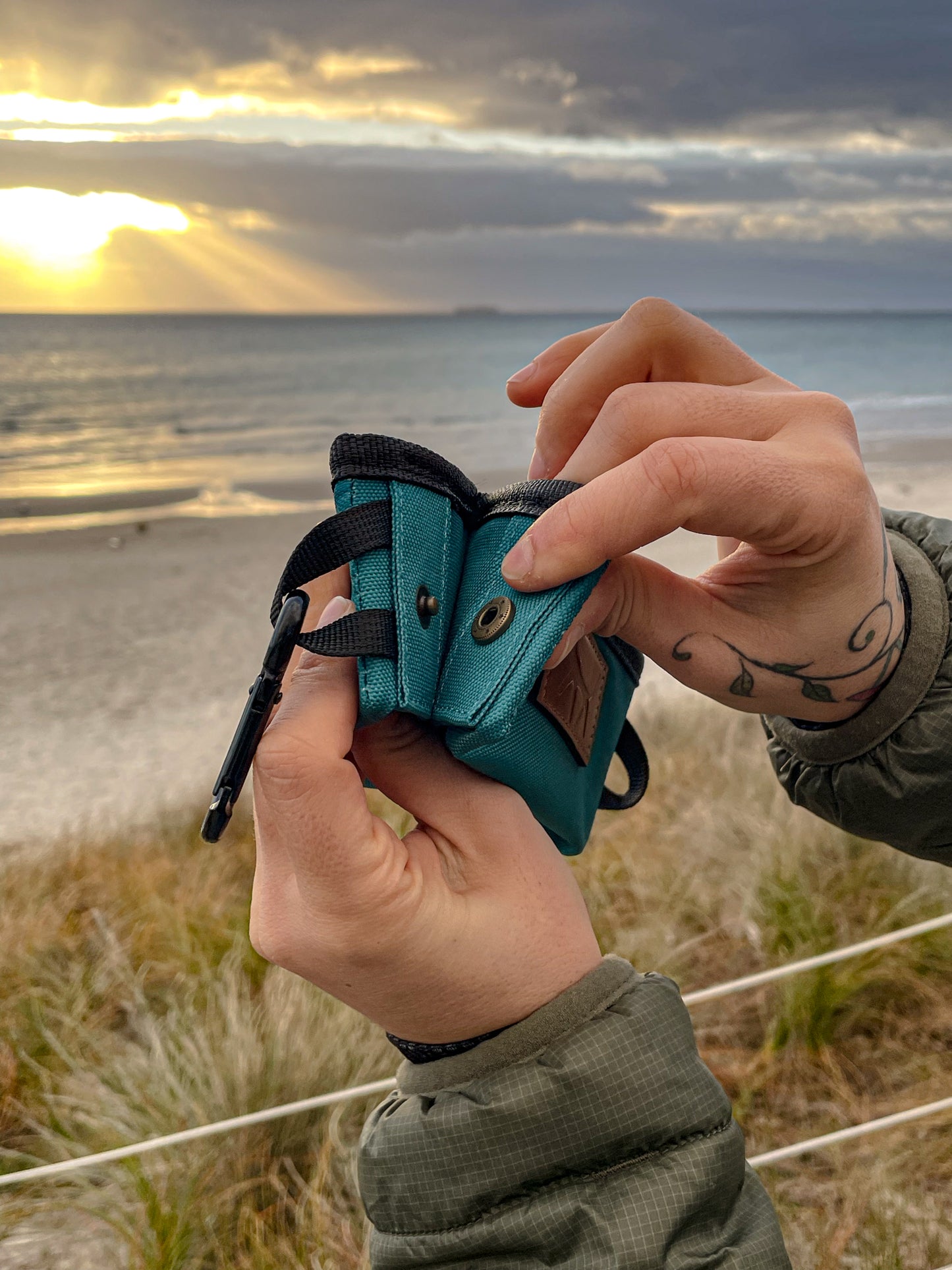 Person hands showing details of the dog travel bowl in lake colour. Sunset scene at the beach as background.