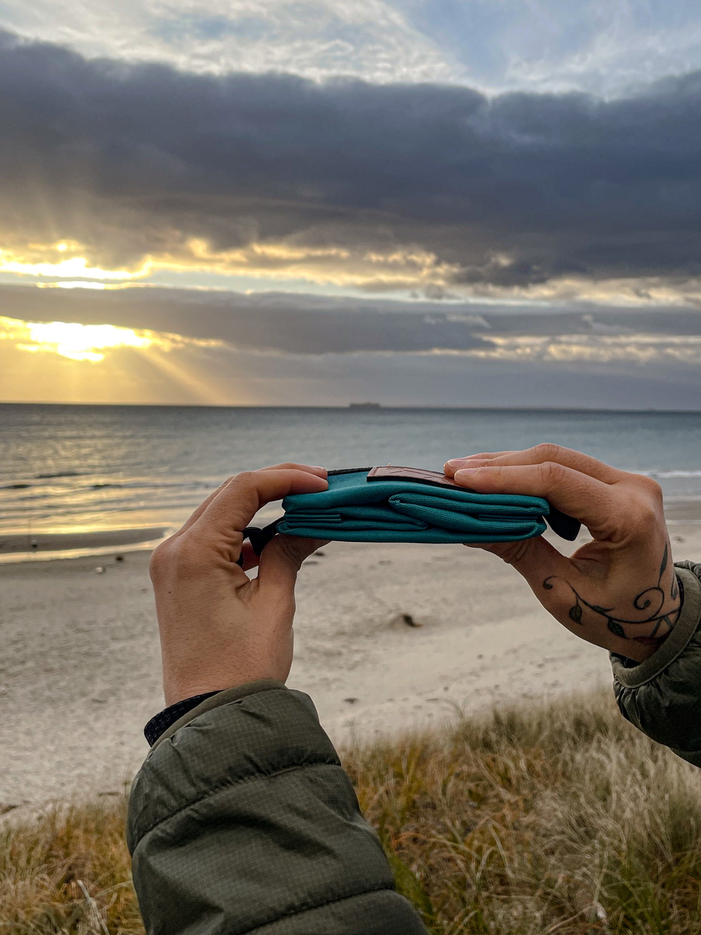 Person showing the dog travel bowl in lake colour folded and how compact it gets. Sunset scene at the beach as background.