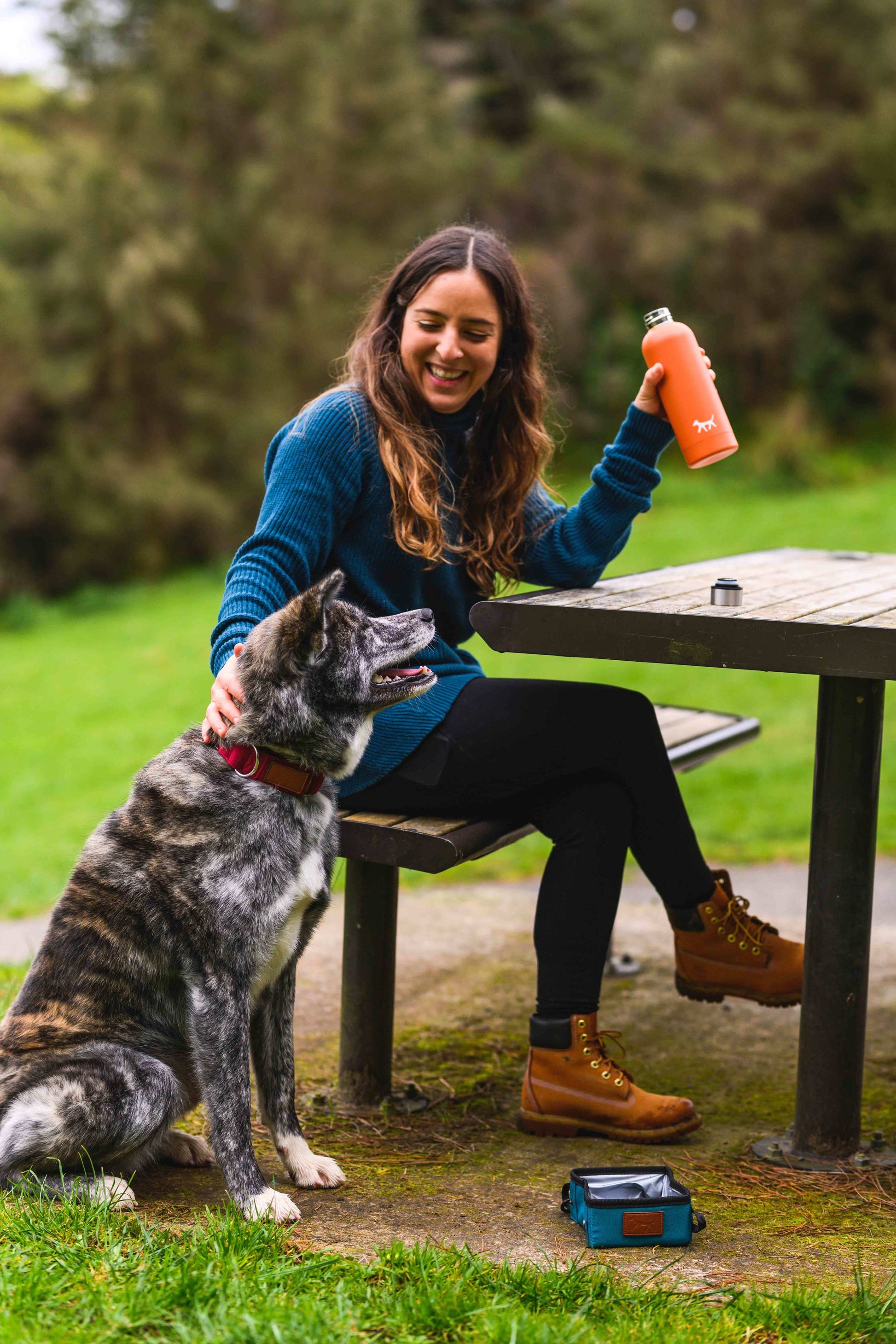 Woman holding a rust Droggo dog water bottle while smiling to her dog